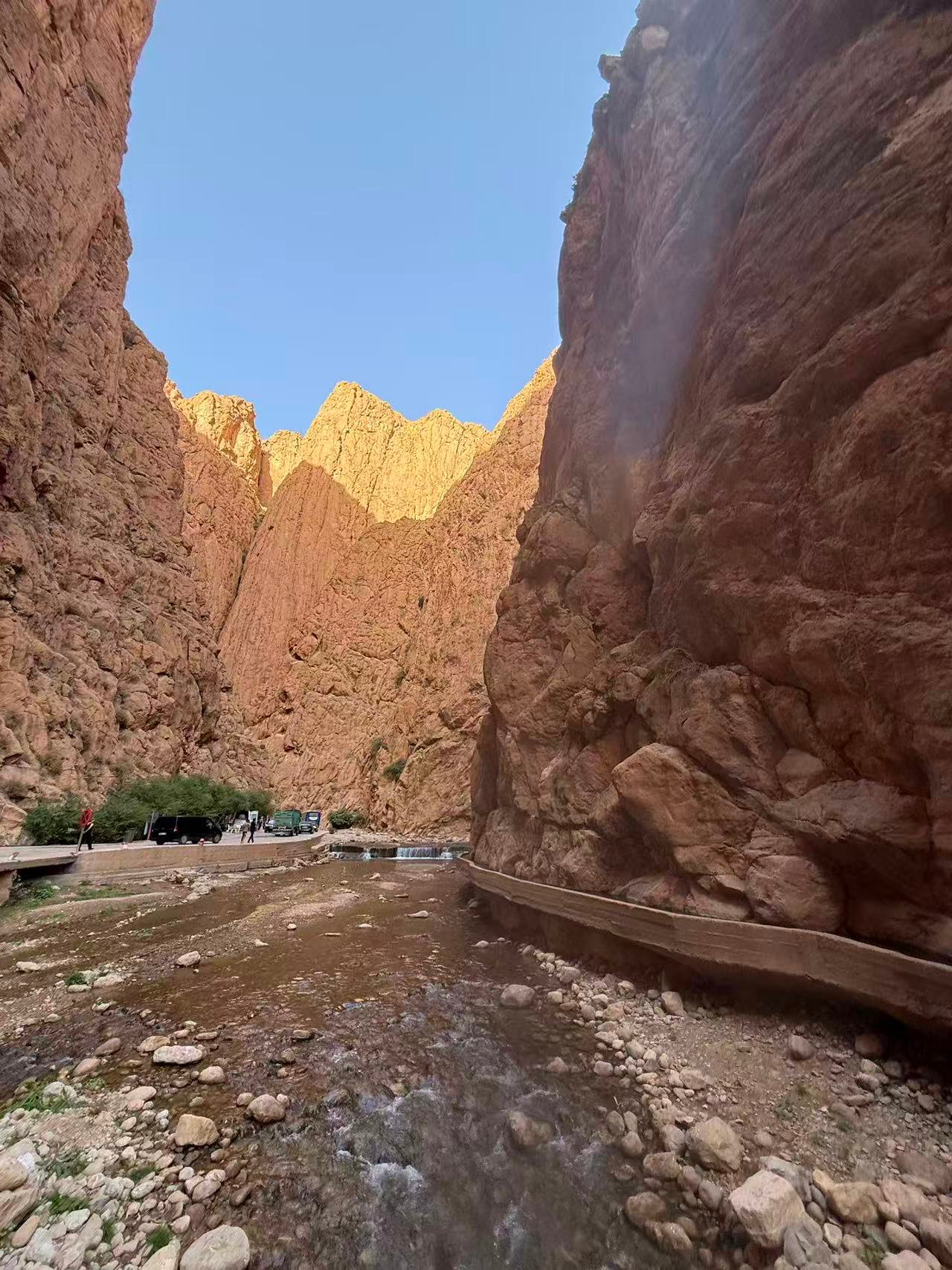 Todgha Gorges narrow canyon Morocco — 300m red rock walls with river at base and hikers